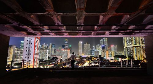 Rear view of man standing at building in city during night