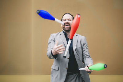 Cheerful businessman juggling bottles against wall