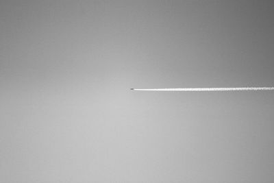 Distant view of airplane emitting vapor trail in clear sky