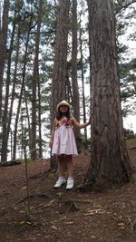 Full length of girl standing by tree trunk in forest