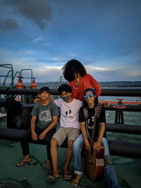 Portrait of friends sitting on shore against sky