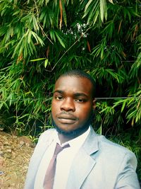 Portrait of young man in suit standing against plants