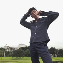 Young man standing on grass against clear sky