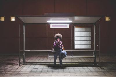 Young woman with afro hairdo using smartphone at bus stop in the city