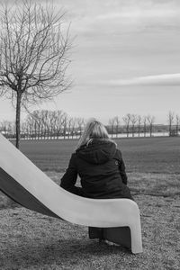 Rear view of woman sitting on seat in field