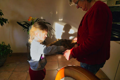 Midsection of grandmother holding cookies in tray while standing with granddaughter at home