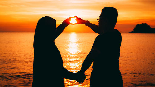 Silhouette couple making heart shape at beach during sunset
