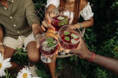 Hands of male and female friends toasting drink glasses at garden party