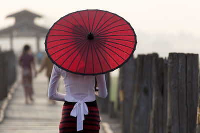 Rear view of woman walking with red umbrella on u bein bridge