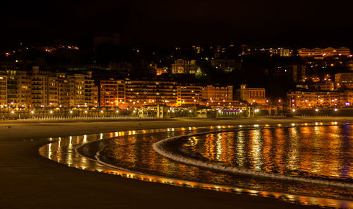 Illuminated buildings by river against sky at night