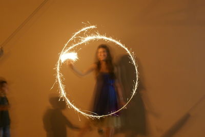 Blurred motion of woman holding illuminated sparkler against wall at night