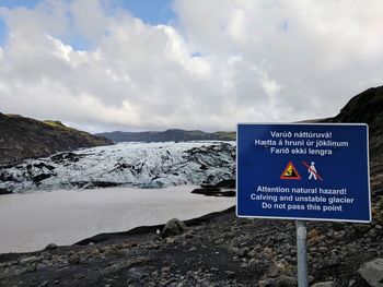 Warning sign on snowcapped mountain against sky