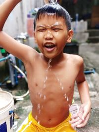 Smiling shirtless boy taking bath outdoors