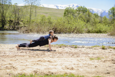 Full length of woman with son doing push-ups on lakeshore