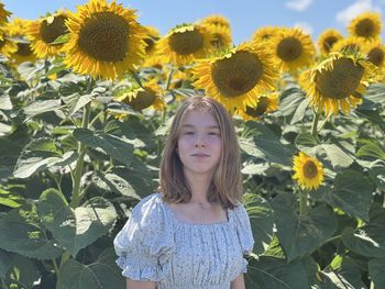 Portrait of young woman standing amidst sunflowers on field