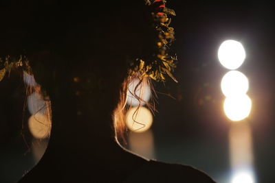 Close-up of silhouette woman against sky and illuminated lights at night