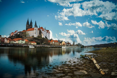 Buildings at waterfront against cloudy sky