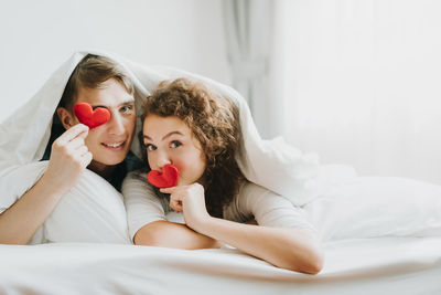 Romantic couple holding heart shapes while lying on bed at home