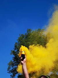 Low angle view of person holding yellow tree against blue sky