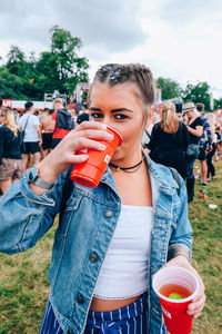 Young woman drinking drink while standing in city during party