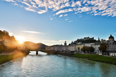 Bridge over river by buildings in city against sky