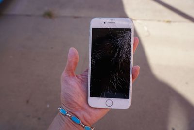 Cropped hand holding broken mobile phone outdoors