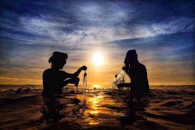 Silhouette people in sea against sky during sunset