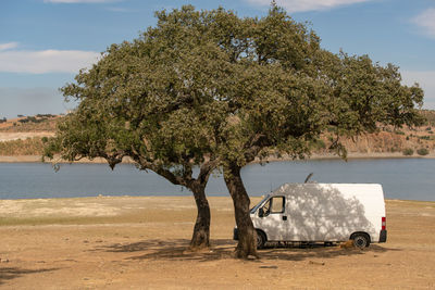 Camper van on an alentejo dam landscape with the lake behind and under the shade of a tree
