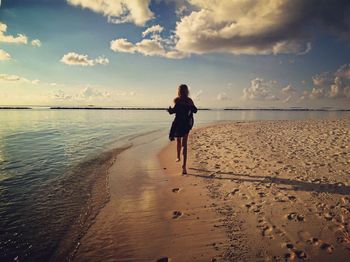 Rear view of sensuous young woman running at beach against sky