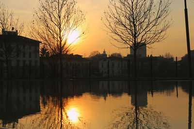 Silhouette buildings by lake against sky during sunset