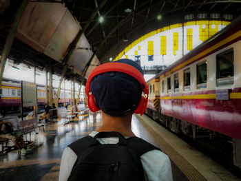 Rear view of boy wearing headphone standing by train at railroad station