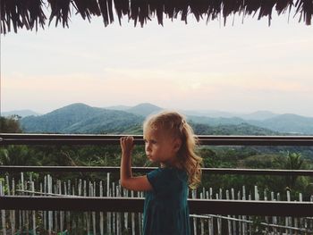 Girl standing by railing against sky