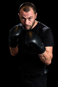 Portrait of mid adult man wearing boxing gloves against black background