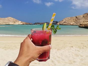 Close-up of hand holding drink at beach