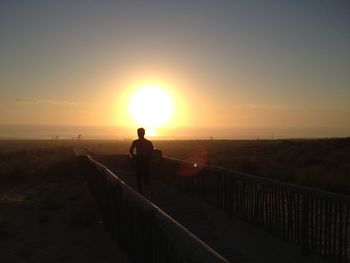 Man standing on railing by sea against sky during sunset