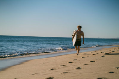 Full length of woman walking on beach against clear sky