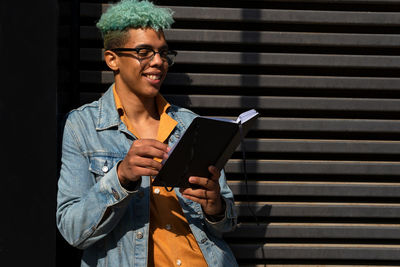 Young woman using phone while standing against wall