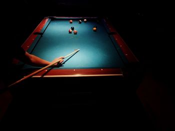 Cropped image of man playing pool in dark