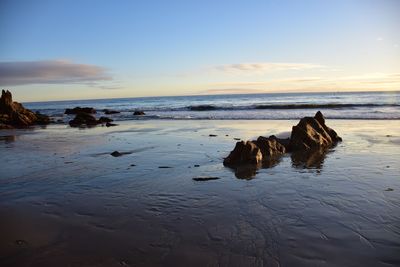 Rocks on beach against sky during sunset