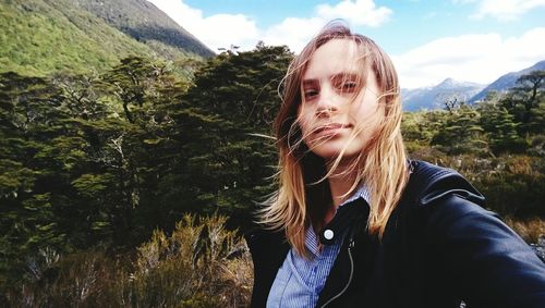 Portrait of beautiful young woman standing against trees