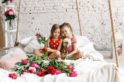 Happy friends sitting on bed by potted plant