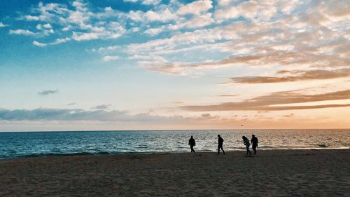 People on beach against sky during sunset