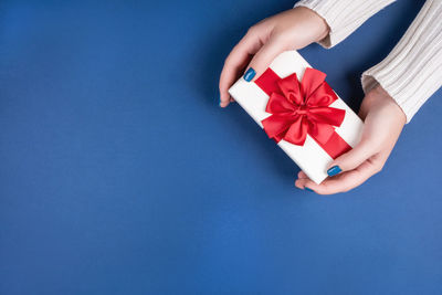 Cropped hand of woman holding gift box against blue background