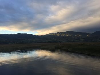 Scenic view of lake and mountains against cloudy sky at sunset