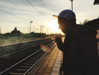 Side view of man smoking while standing at railroad station platform