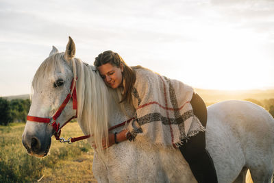 Young woman embracing while riding white horse during sunset