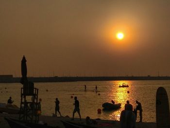 Silhouette people by sea against sky during sunset