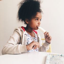 Girl eating popsicle against wall at home