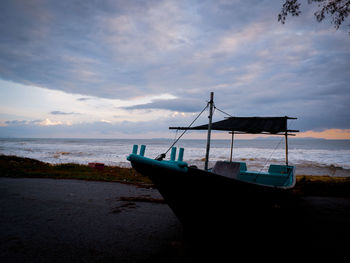 Boat moored on beach against sky during sunset