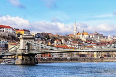 Bridge over river by buildings in city against sky